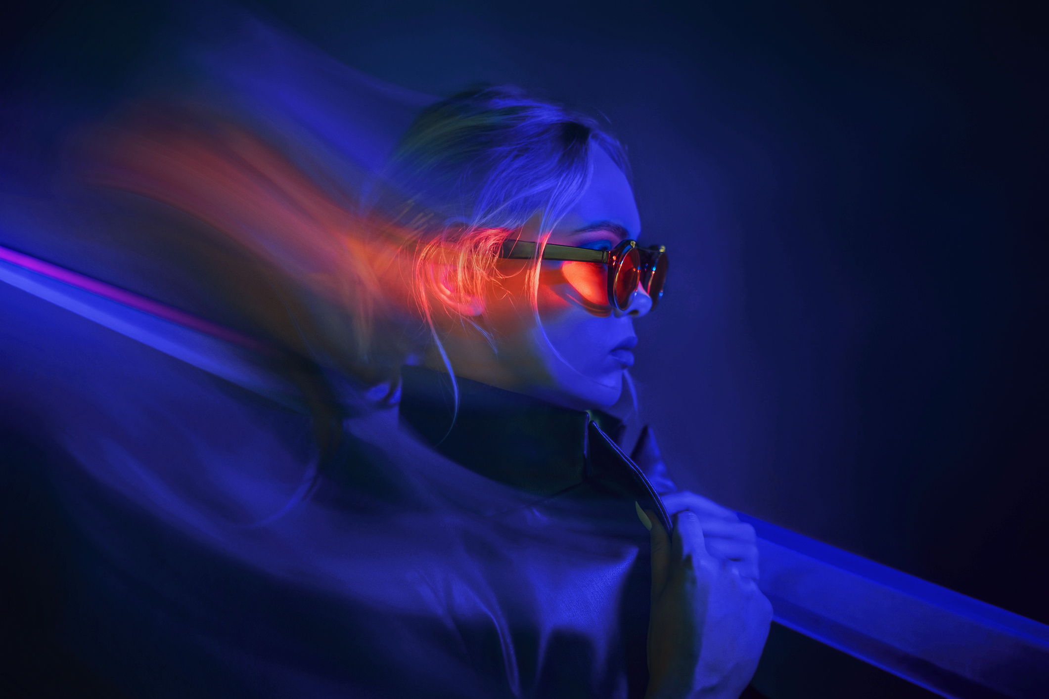 Portrait de mode en studio, éclairage néon bleu et rouge avec filé de lumière, lunettes teintées.