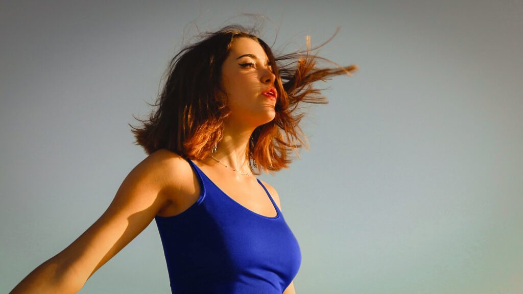 Portrait féminin en lumière naturelle, chevelure en mouvement, illustrant la retouche naturelle qui préserve le grain de peau